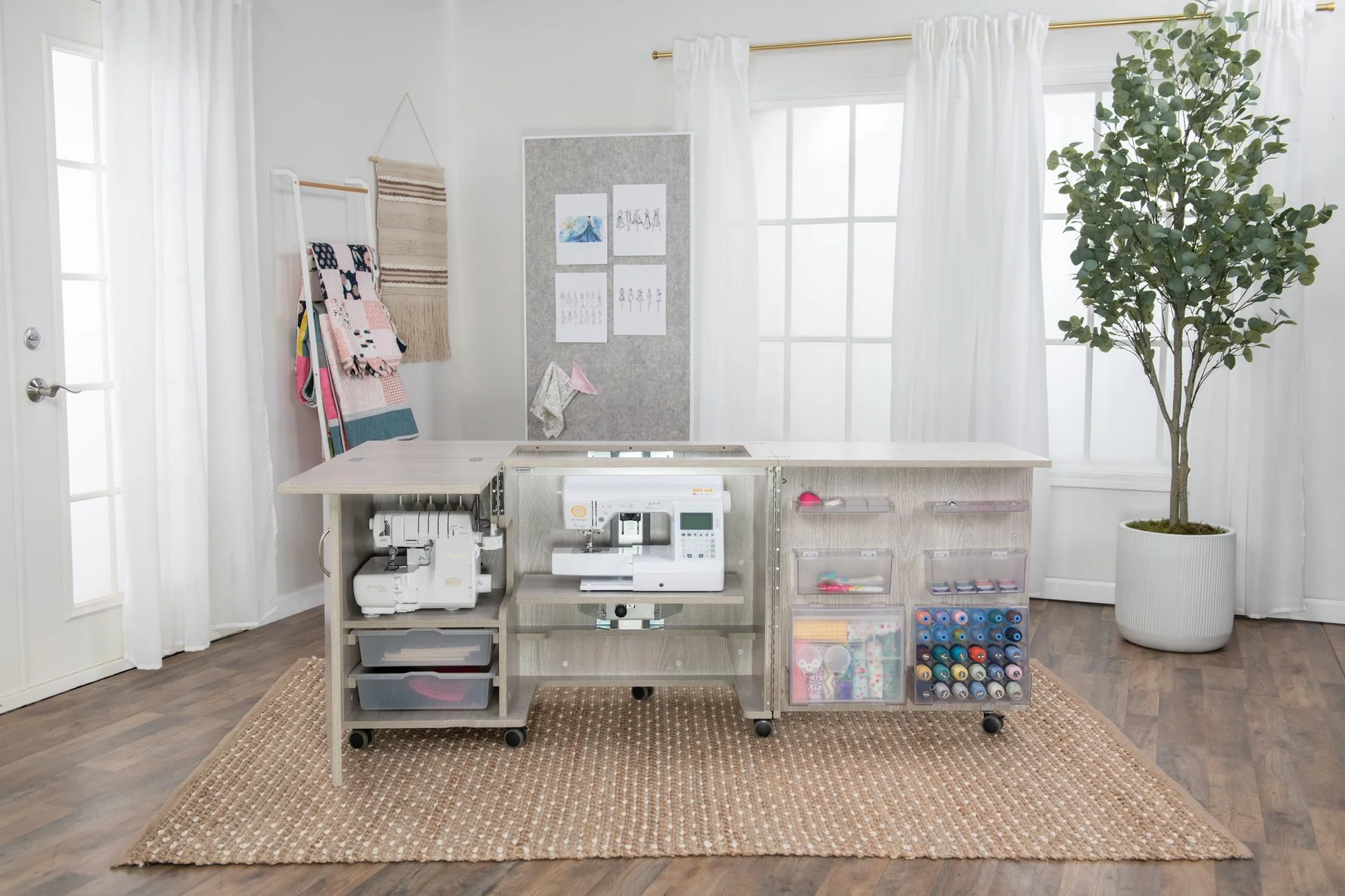 A compact fold-out sewing table opened in a small apartment living room with a chair positioned for sewing, showing clear walking space around the setup