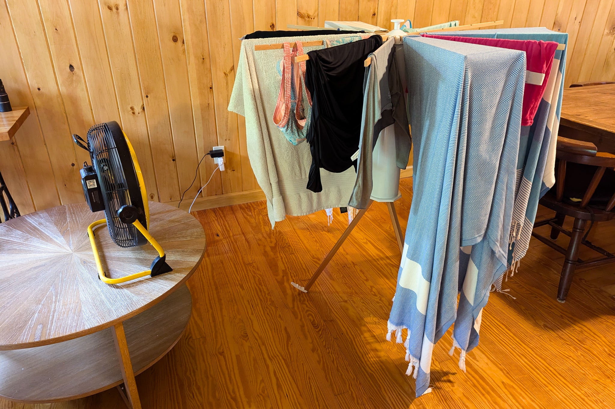A small studio apartment with a fold-away drying rack set up near a window, clothes spaced evenly on the rails, and clear walking space around the rack