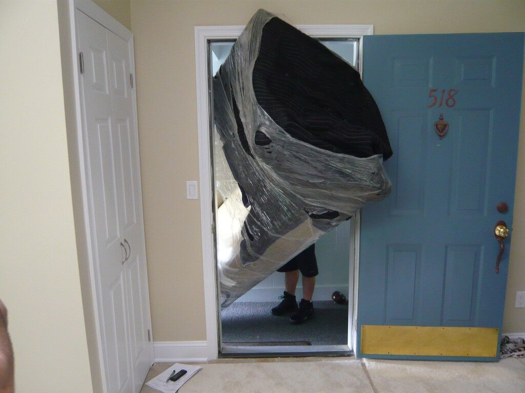 Two movers carrying a boxed sofa up a narrow apartment stairwell with a tight landing turn.